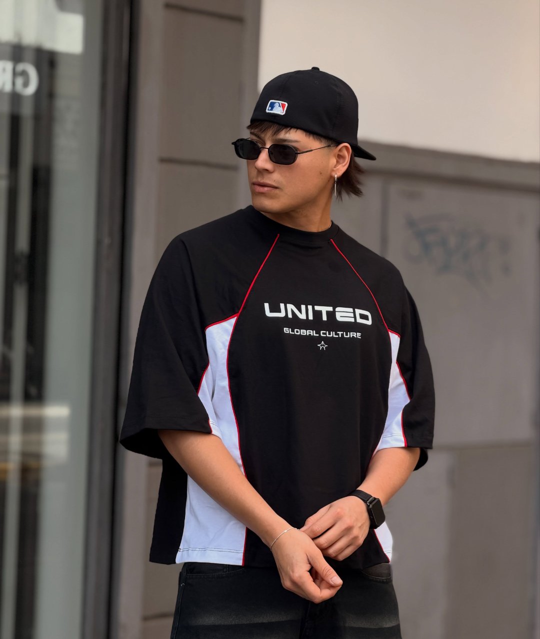 Remera boxy United negra con paneles blancos y vivos rojos, gorra negra y lentes